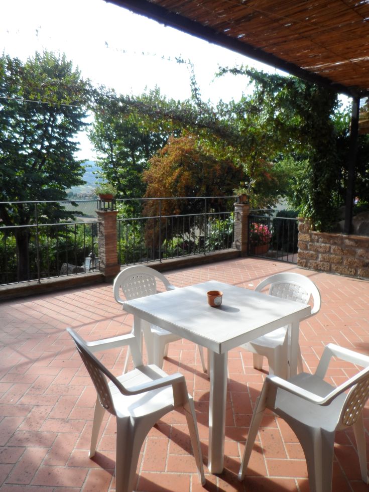 Un terrazzo luminoso con tavolo e sedie, circondato dalla natura e affacciato su un panorama sereno.