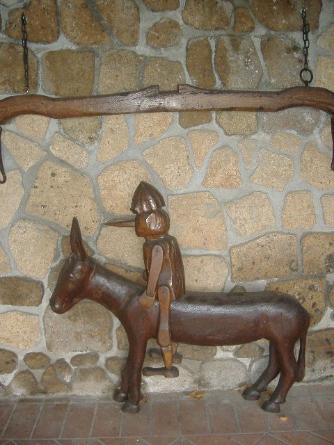 Scultura in legno raffigurante un personaggio in sella a un asinello, esempio di artigianato tradizionale in un ambiente semplice.