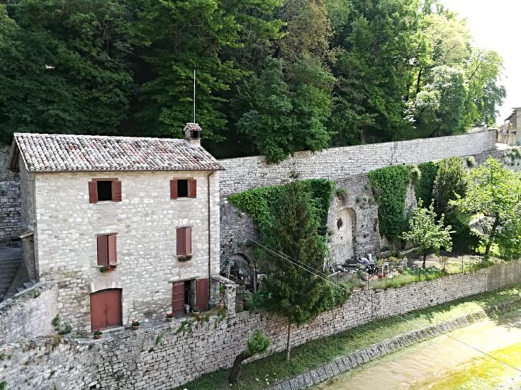 Un edificio medievale circondato da alberi, che si affaccia su un corso d'acqua chiamato torrente Camignano.