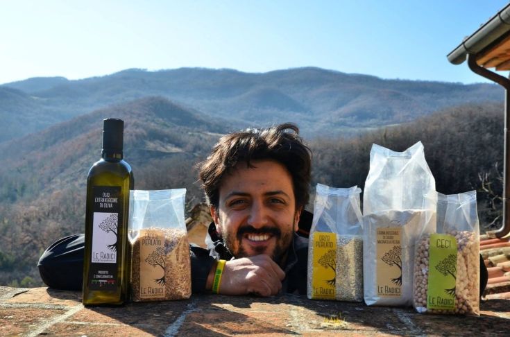 Un ragazzo sorridente si trova tra prodotti tipici locali, circondato da un paesaggio umbro.