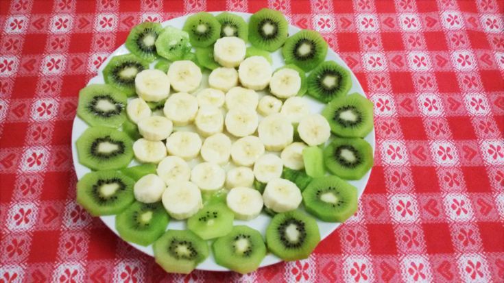 Ein Tablett mit verschiedenen Scheiben Kiwi und Banane, die auf einer roten Tischdecke angeordnet sind.