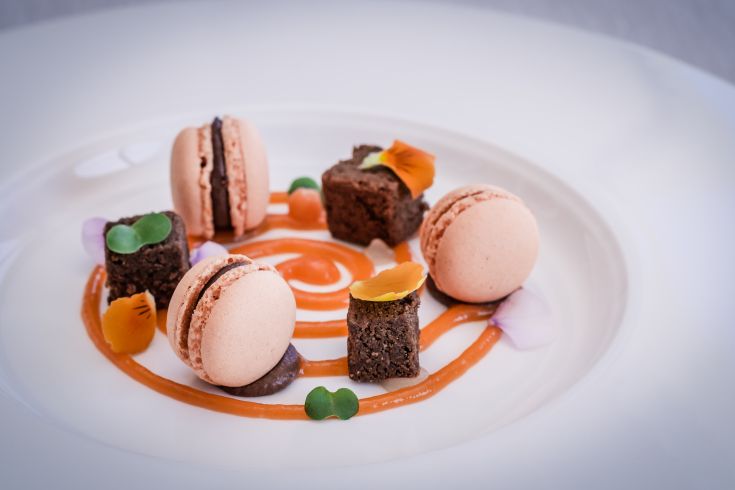 Un dessert composto da macaron e cubetti di torta, servito su un piatto semplice ma curato.