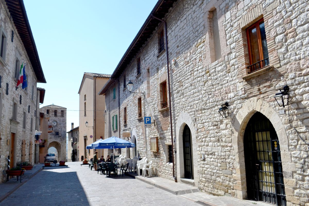 Una tranquilla strada in un borgo medievale, circondata da edifici in pietra e arredi semplici all'aperto.