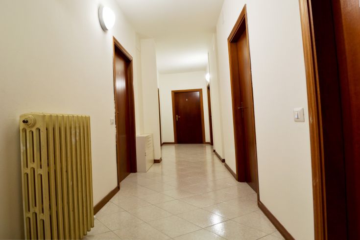 A bright corridor with brown wooden doors and a radiator on the left.