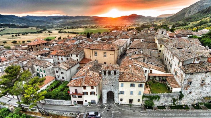 A scene of a medieval village at sunset, surrounded by gentle green hills and the typical tranquility of the Umbrian landscape.