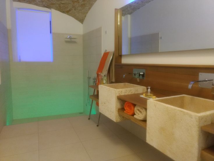 Bagno moderno con doccia e lavabo in pietra, arredato con toni chiari e una luce soft.
