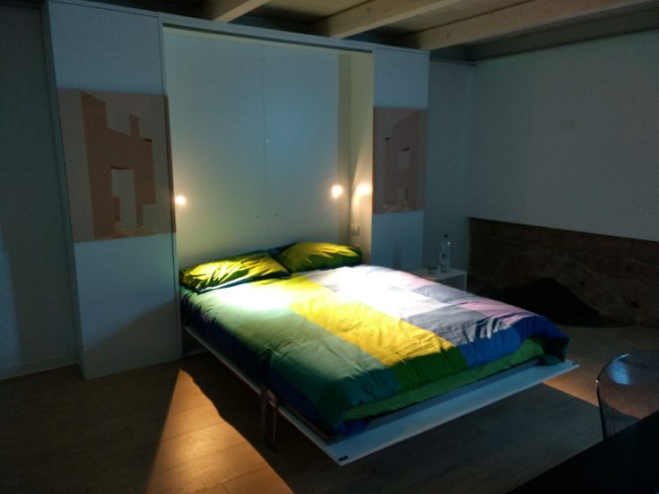 Camera moderna con un letto dai colori vivaci e una luce soft, inserita in un ambiente confortevole.