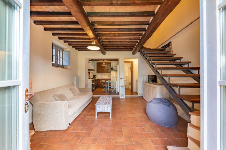 Interno di un edificio con travi a vista, un soggiorno e una cucina luminosa.
