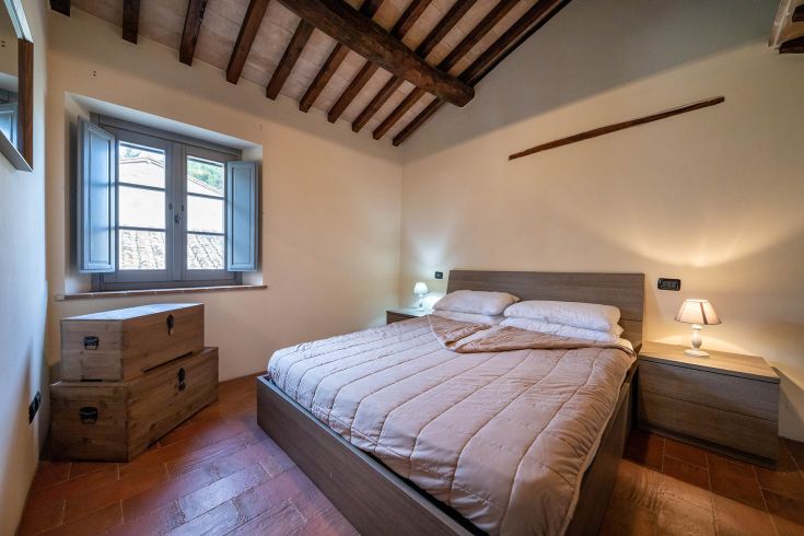 Camera semplice in un palazzo, con travi in legno e finestre che lasciano entrare la luce naturale.