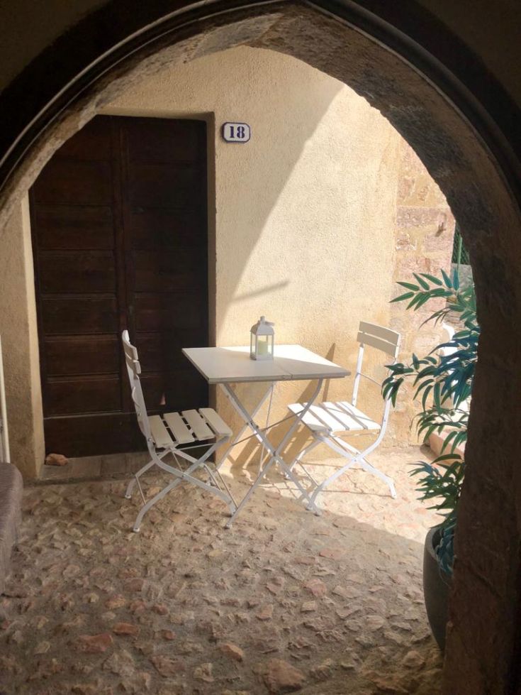 A white table with chairs sits in a cozy corner, surrounded by stone walls.
