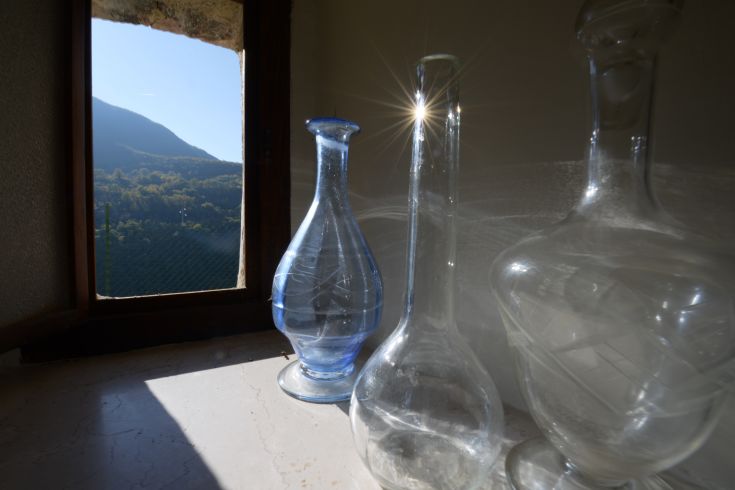 Three glass bottles placed on a windowsill, overlooking a surrounding mountain landscape.