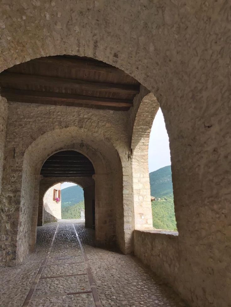 A stone corridor with arches, surrounded by natural vegetation.