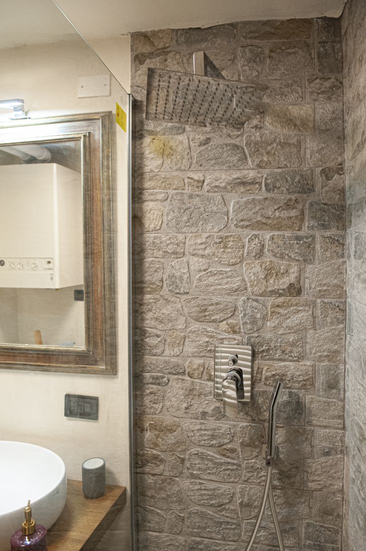 A modern bathroom with stone walls and a contemporary ceiling. Features a rain shower and a stylish sink.