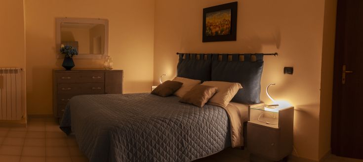 A simple bedroom with double beds and minimal furnishings, lit by warm light lamps.