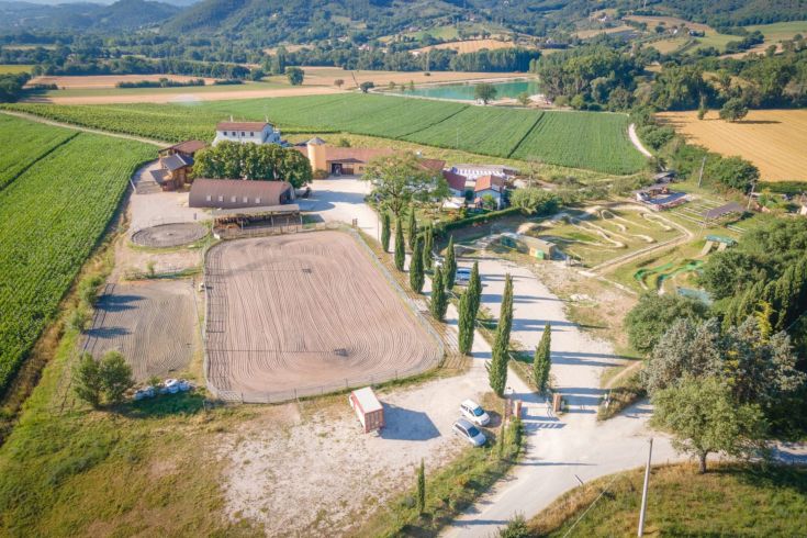 A panoramic view of a farm surrounded by vineyards and gentle green hills.