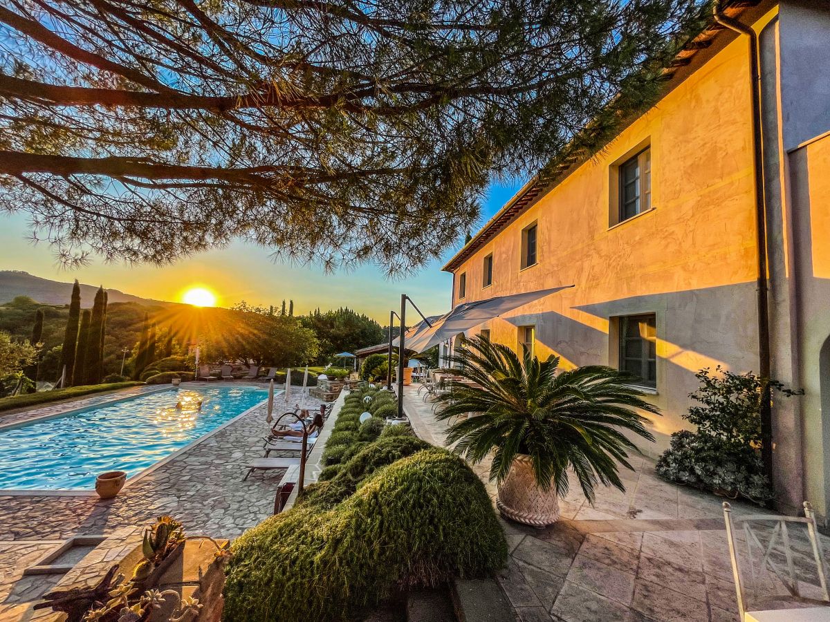 Ein Sonnenuntergang spiegelt sich im Pool eines Gebäudes, das in einer natürlichen Umgebung mit grünem Pflanzenbewuchs steht.