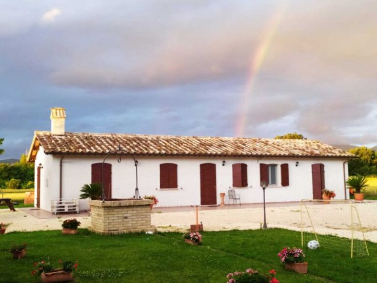 A villa surrounded by greenery, with plants and flowers, under a clear sky with a rainbow.