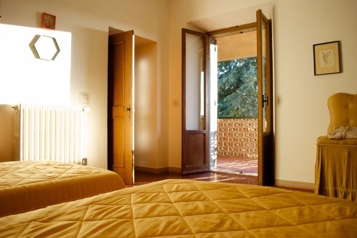 Gemütliches Zimmer mit gelben Betten und Blick auf eine Terrasse, umgeben von Grün.