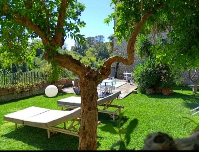 Giardino curato con lettini e una piscina circondata da alberi, situato in un borgo medievale.