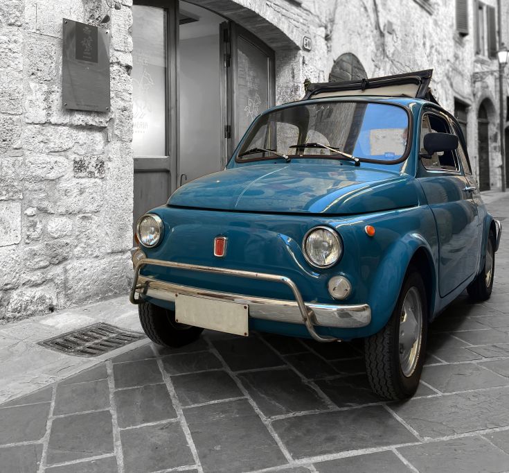 Une voiture ancienne bleue garée dans une ruelle tranquille d'un ancien village ombrien.