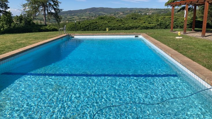 Détente au bord de la piscine au milieu de la verdure de l'Ombrie, entourée d'arbres et de champs.