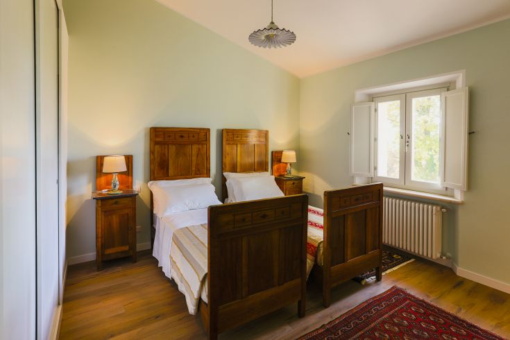 Chambre rustique avec lits simples et lampe, donnant sur un paysage verdoyant. Espace accueillant et relaxant.