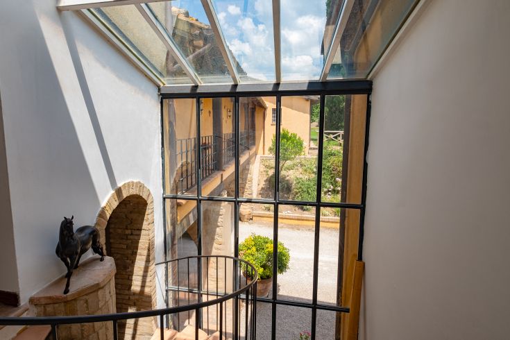 Intérieur d'un bâtiment avec un escalier et une vue sur une cour. Lumière naturelle et détails architecturaux simples.