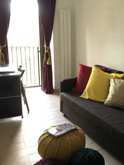 A bright living area with a colorful sofa, vibrant cushions, and large windows letting in natural light.