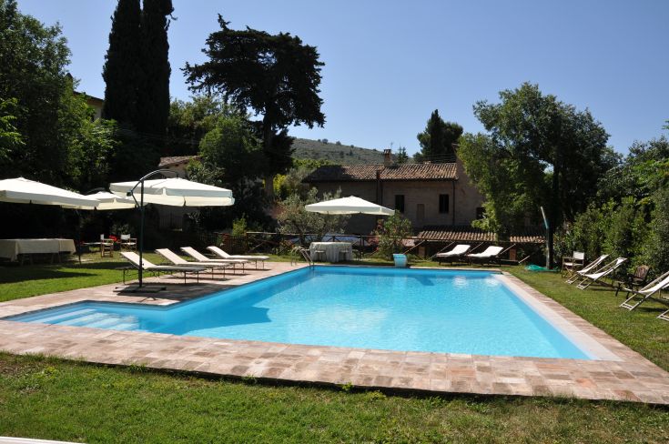 Swimming pool surrounded by lush green spaces and traditional Umbrian architecture.