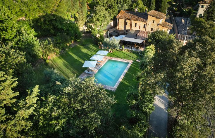 A scene of a pool surrounded by green trees and an ancient farmhouse in the background.