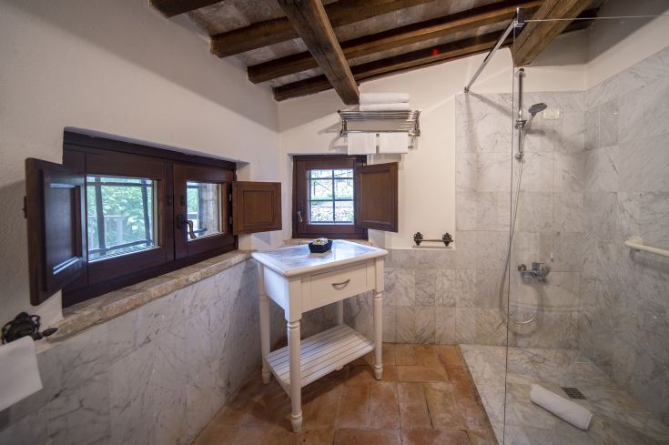 A simple bathroom with marble walls and a window overlooking a well-kept garden.
