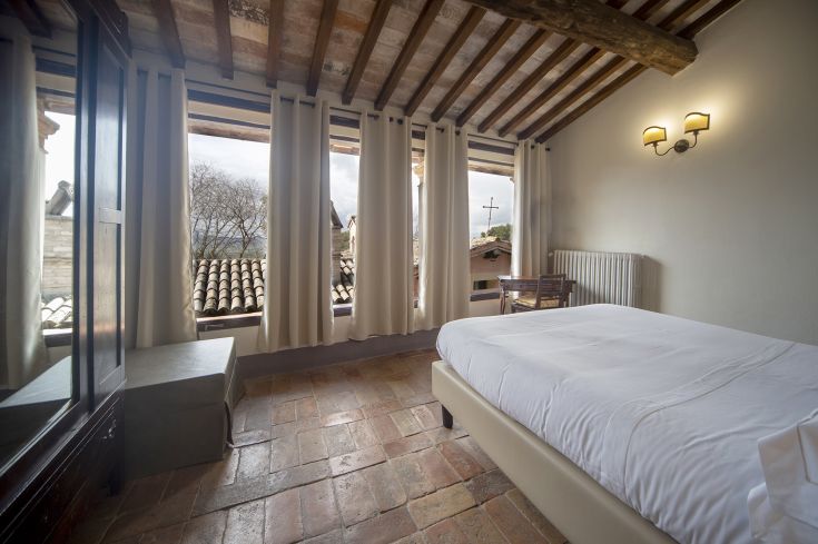 Simple room with terracotta flooring and exposed beams, overlooking a countryside view.