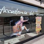 Un giovane uomo salta con una valigia, pronto per partire. Sullo sfondo, dei cartelli mostrano indicazioni per vari luoghi.