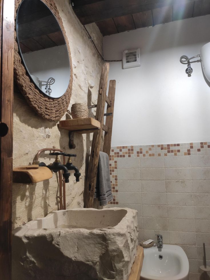 Interno di un bagno rustico con lavabo in pietra e specchio circolare. Ambiente rilassato e semplice.