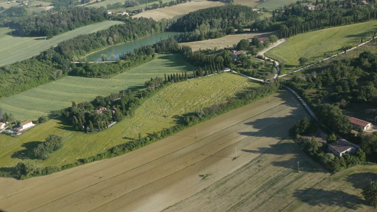 A wide view of the Umbrian countryside, featuring green fields and a serene stream.