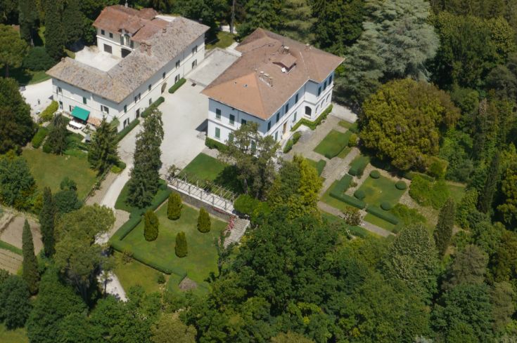 Villa surrounded by large green spaces, featuring well-maintained gardens and nearby buildings.