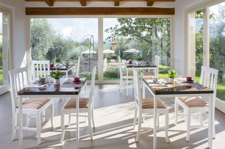 Elegant restaurant with stylish decor, neatly arranged tables, surrounded by green plants, overlooking a bright garden.