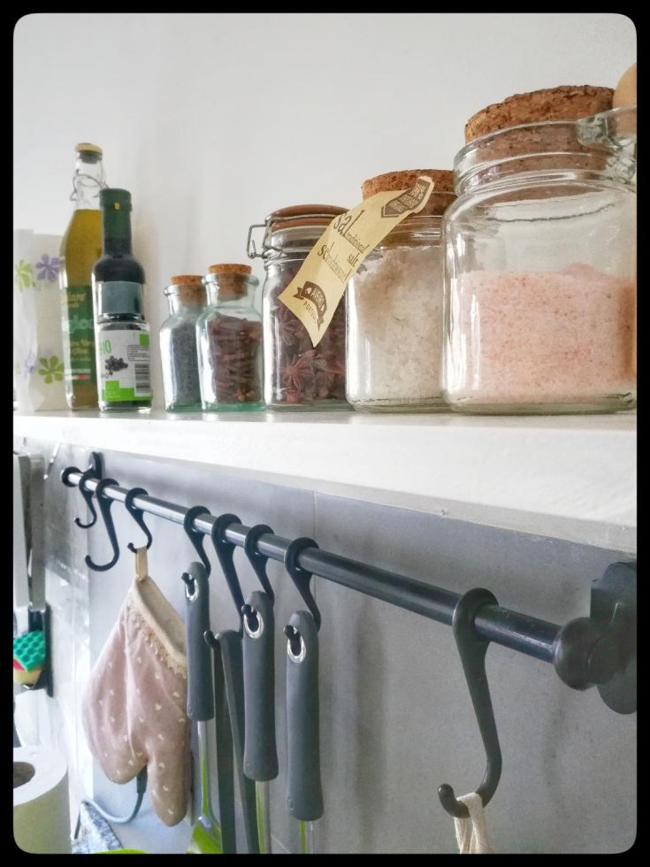 Una cucina ben organizzata con barattoli in vetro per spezie e utensili appesi, creando un'atmosfera rilassata.