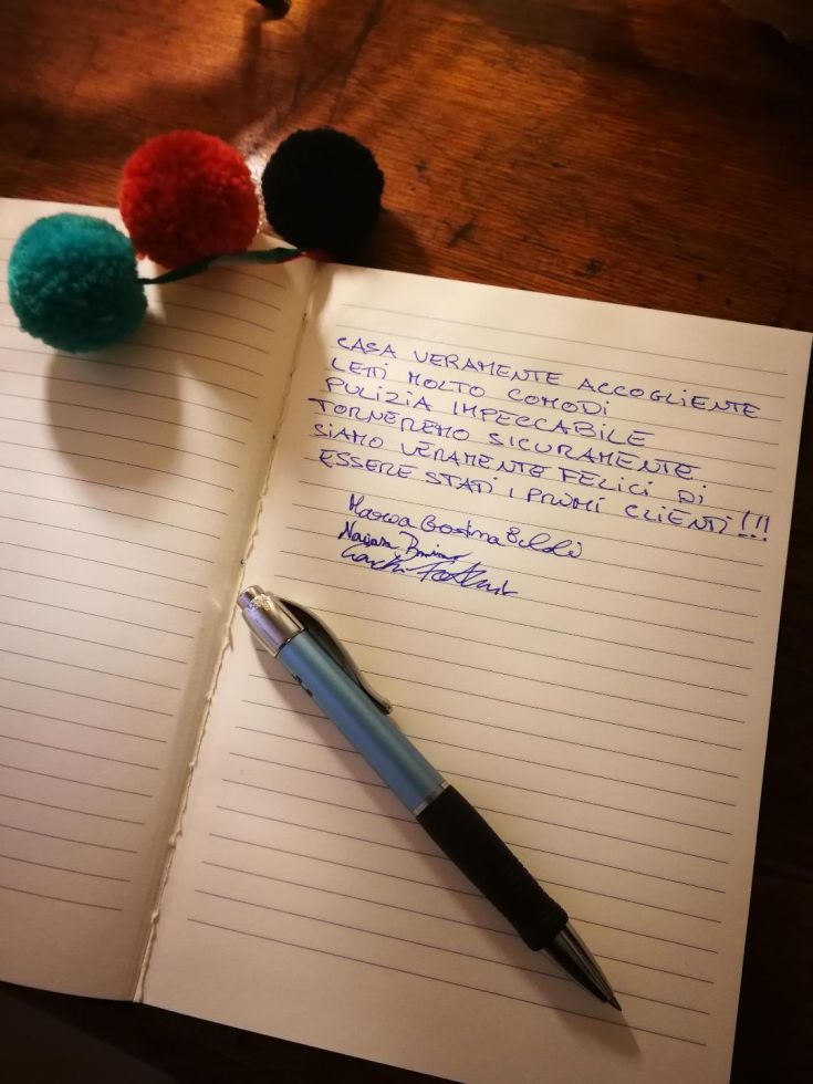 Quaderno aperto con una recensione scritta a mano, che descrive un soggiorno ordinato e piacevole. Elementi decorativi visibili nel contesto.