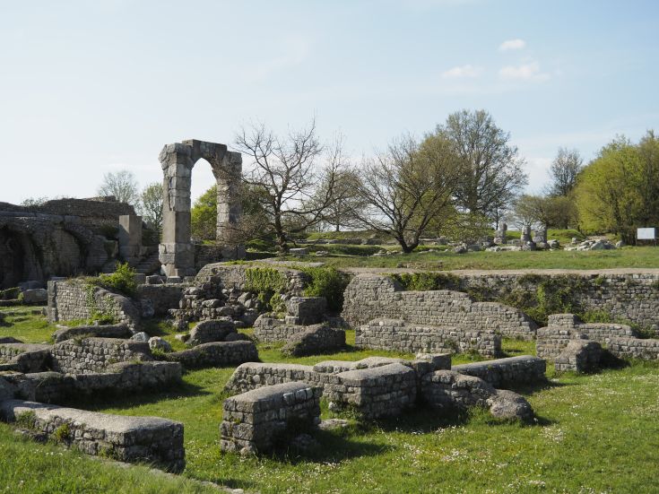 Historic ruins surrounded by greenery, featuring arches and ancient stones under a clear sky.