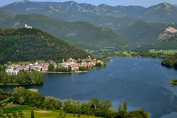 A panoramic view of a lake surrounded by hills and a peaceful nearby settlement.