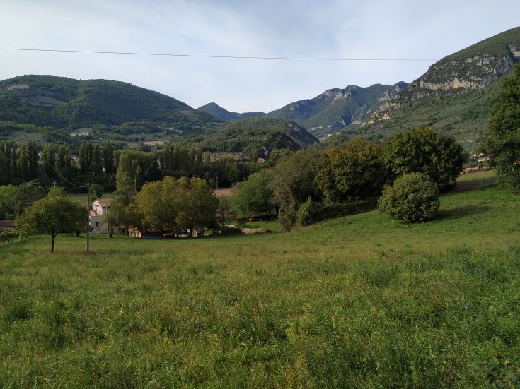 Hilly landscape with green vegetation and some houses, set in a natural environment.