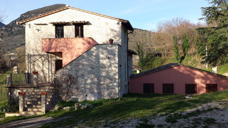 A serene stone villa nestled in nature, surrounded by trees and gentle hills.