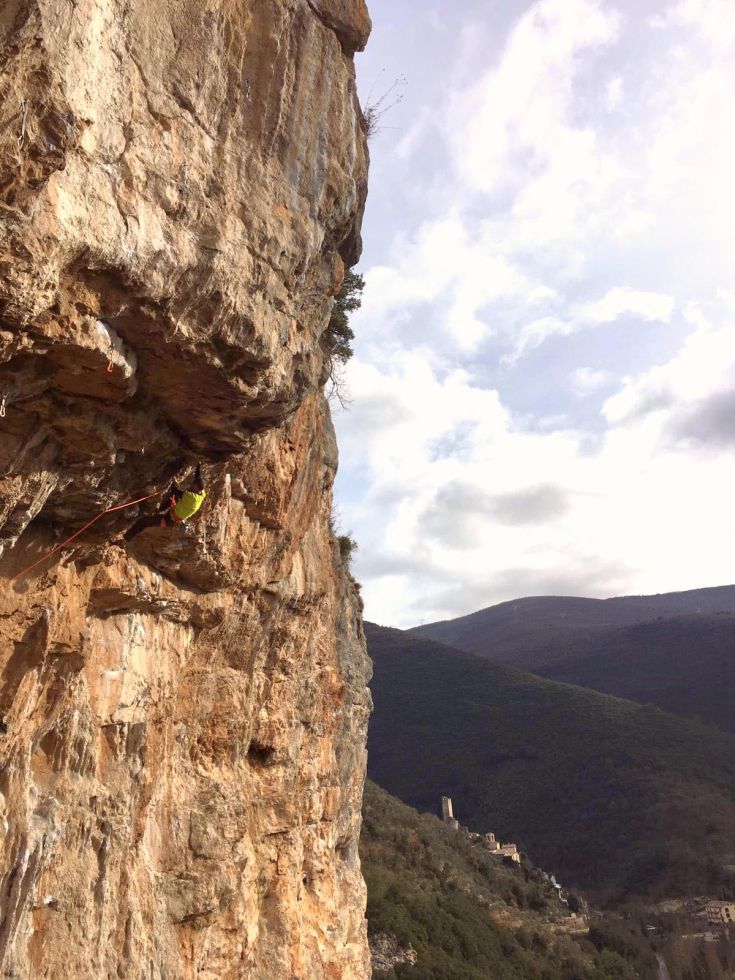 A climber ascends a rocky wall surrounded by a natural environment.