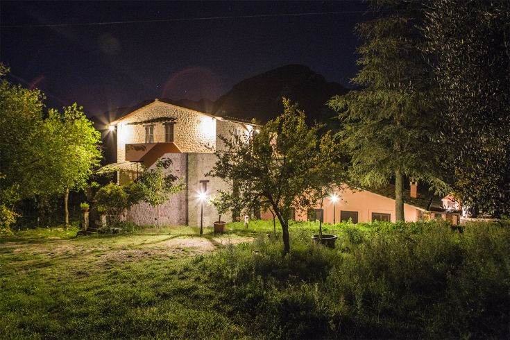 A villa illuminated at night, surrounded by lush trees and vegetation.