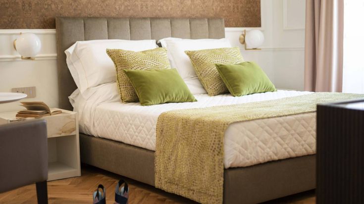 Camera spoglia con letto matrimoniale, cuscini verdi e mobili semplici.