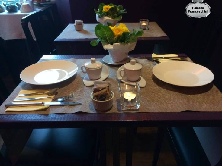 Tavolo apparecchiato con piatti bianchi e decorazioni sobrie, pronto per il pranzo.