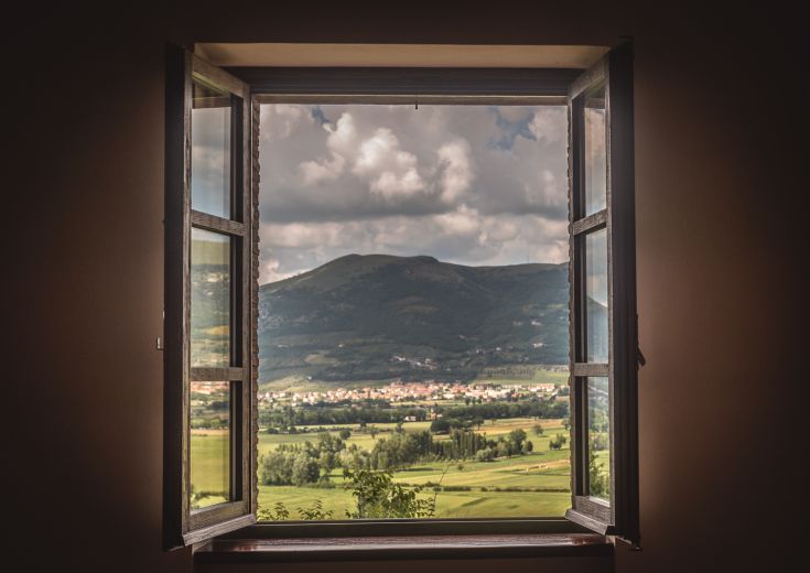 Panorama montano visibile da una finestra, con un paesaggio verde e nuvole in lontananza.