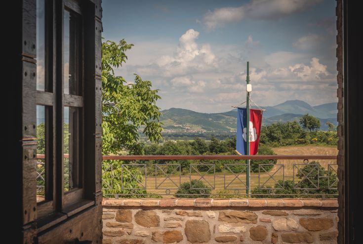 Scena dalla finestra di un agriturismo con bandiera, immerso nella natura circostante.