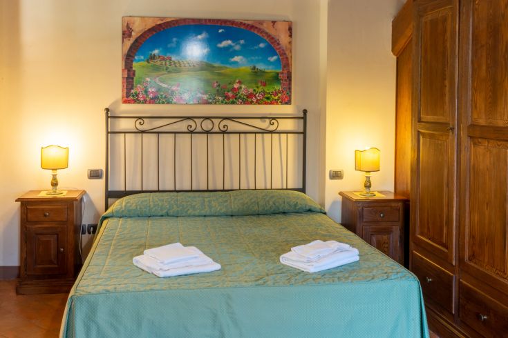 Camera confortevole con letto matrimoniale, illuminazione morbida e un'opera decorativa sulla parete.